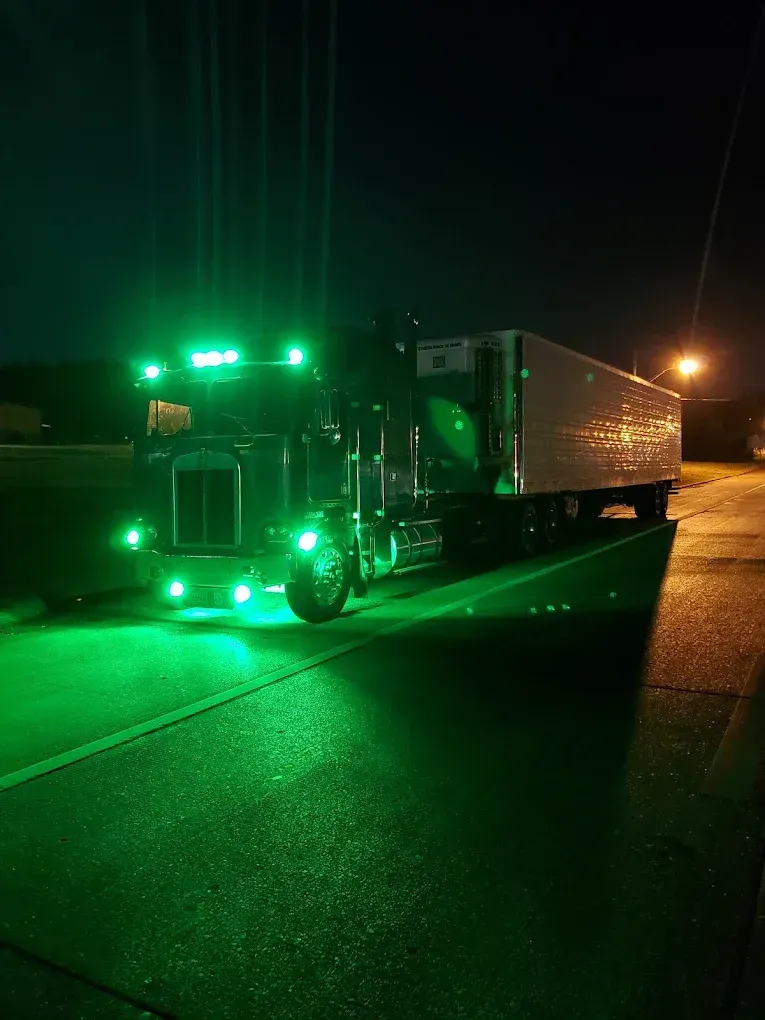 A semi truck is parked on the side of the road at night with green lights on.