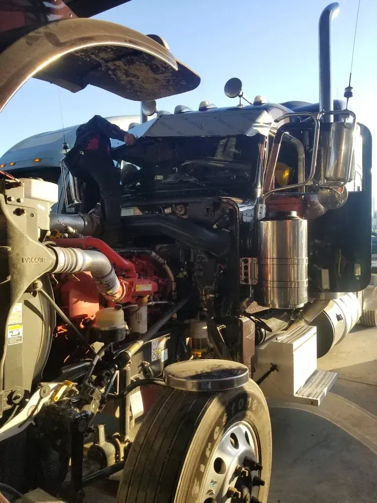 A semi truck with its hood up is being worked on