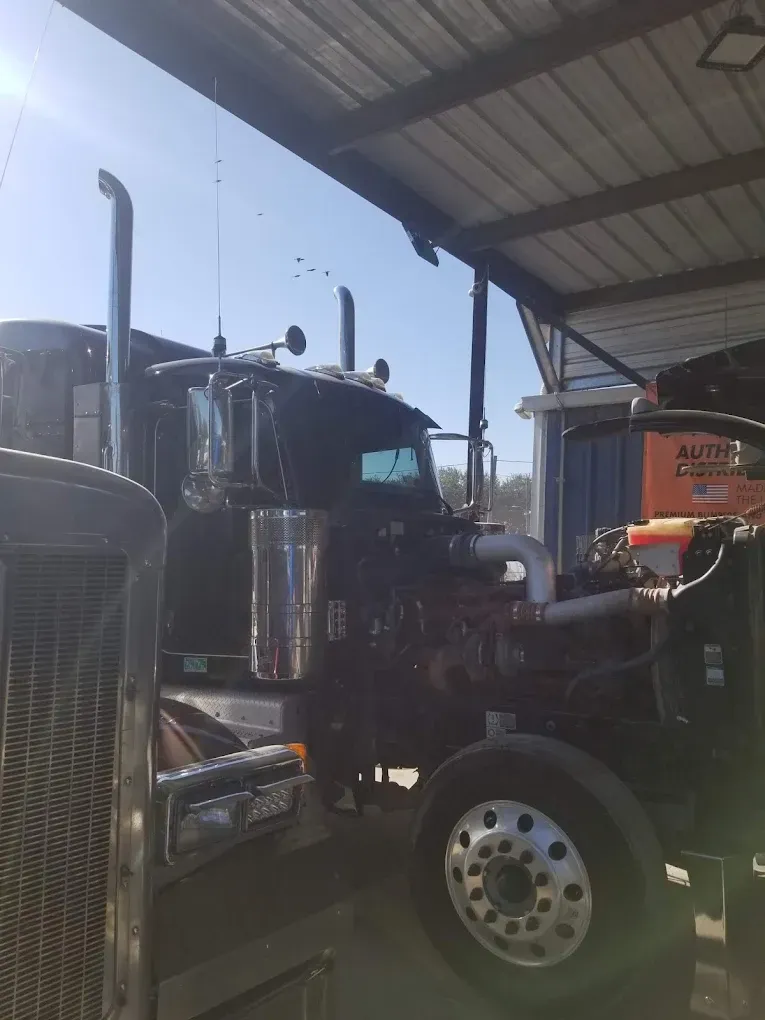 Two semi trucks are parked under a roof in a garage