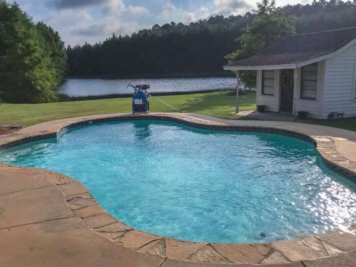 A large swimming pool with a house in the background and a lake in the background.