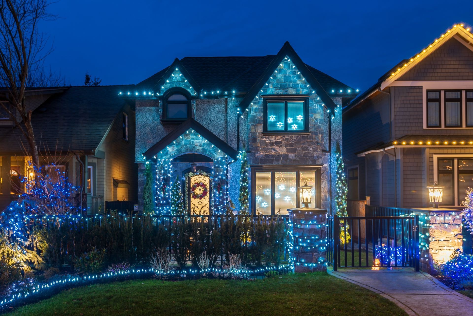 House covered in blue Christmas lights at dusk, wreath on door.