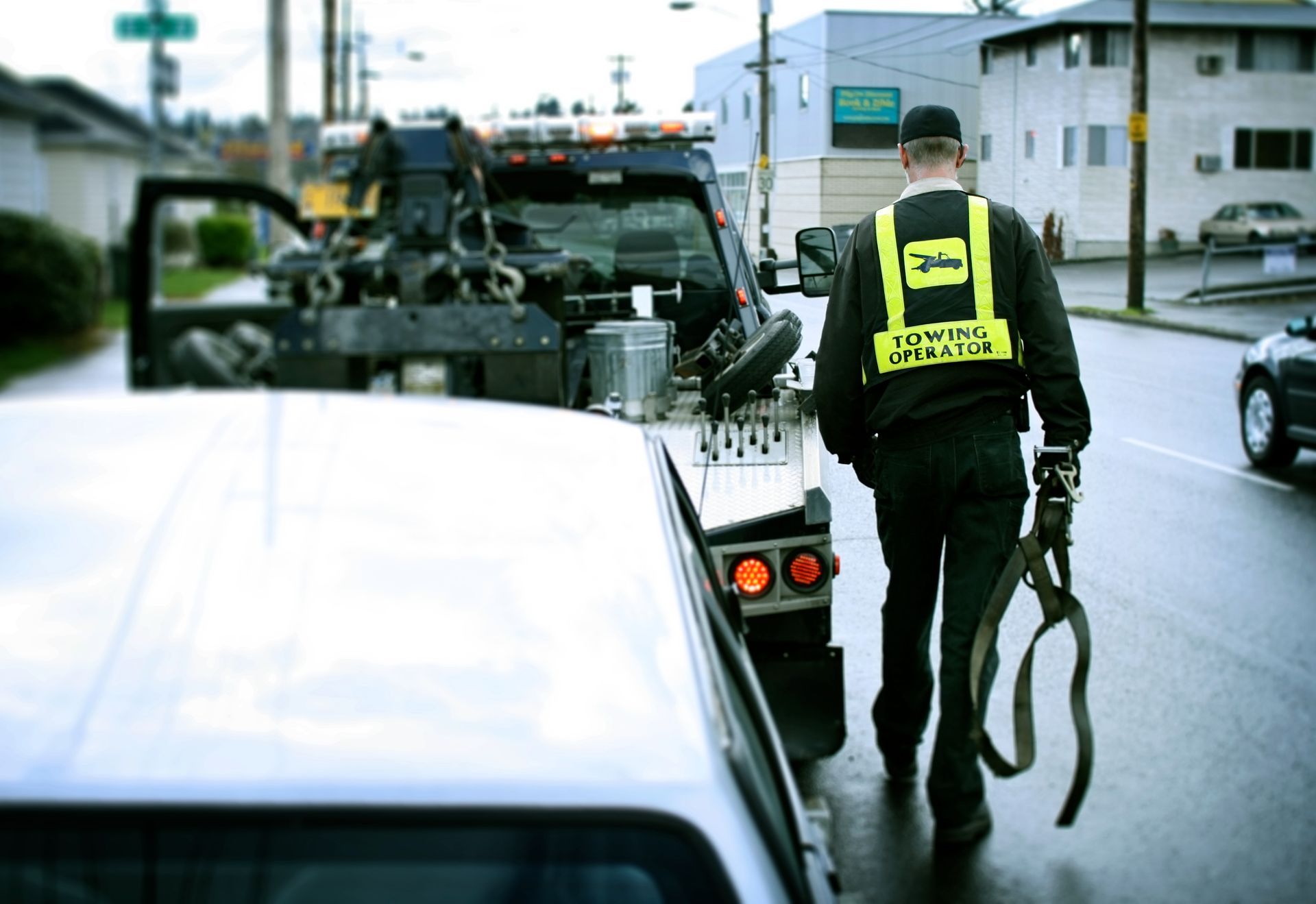 A roadside assistance professional on the job hooking up a broken down car to his tow truck