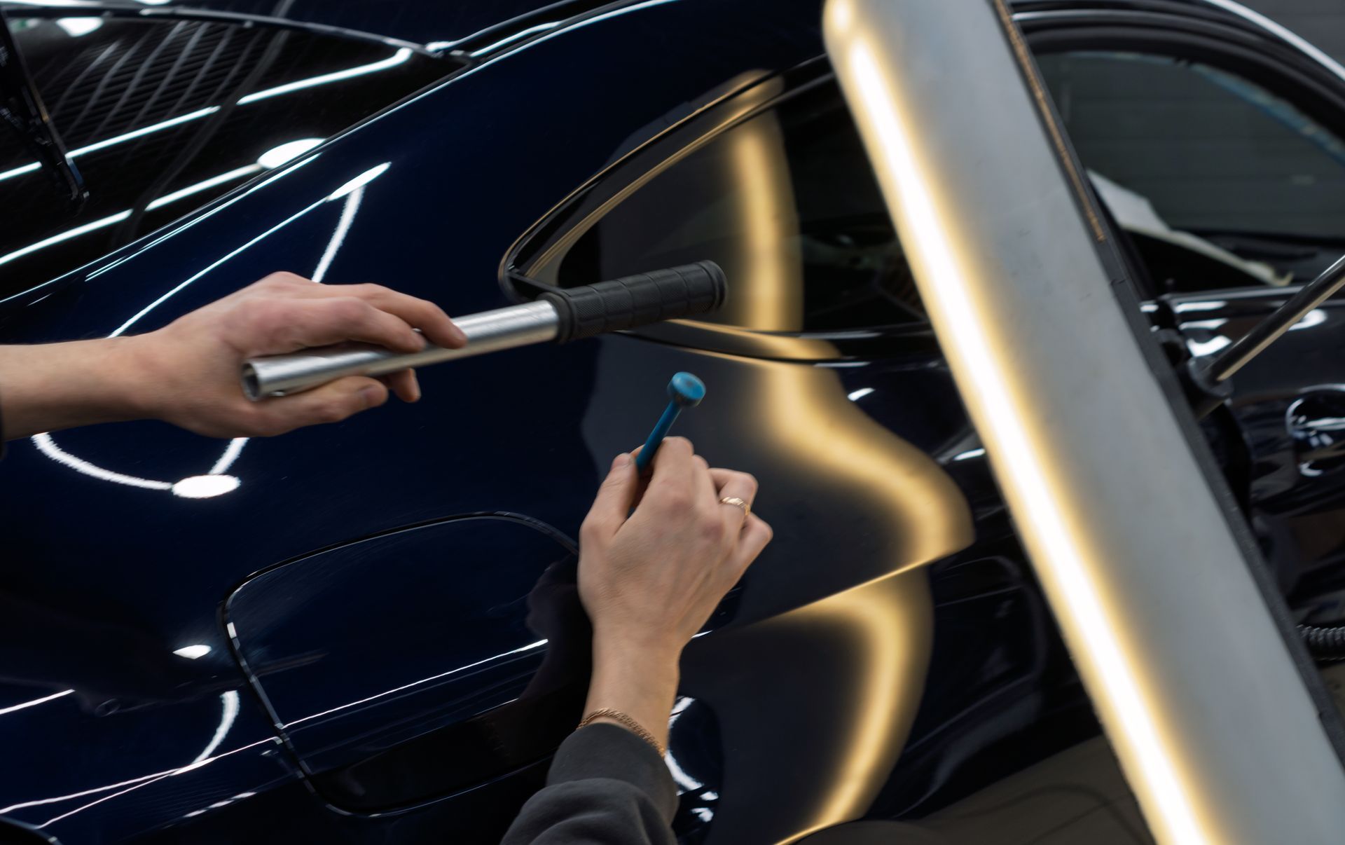 Technician performing paintless dent repair on dark car panel. Technician performing paintless dent repair on dark car panel.