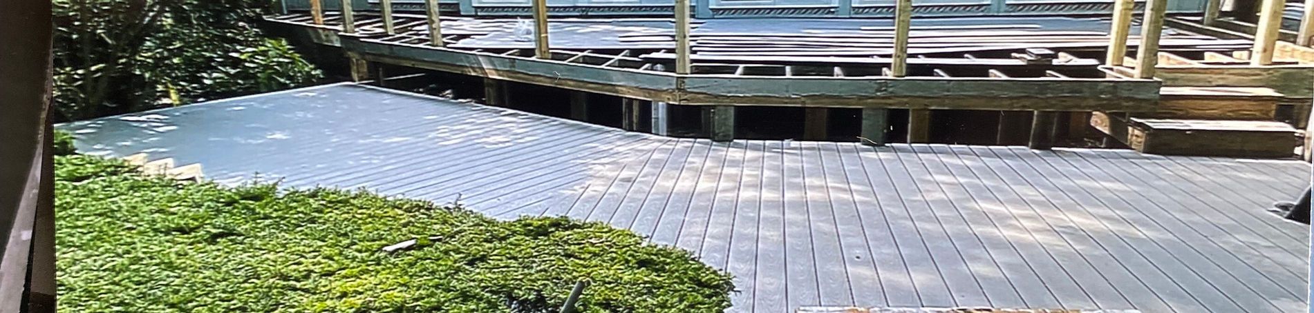A gray brick patio with a circular pattern next to a raised wooden deck with steps and garden greenery.