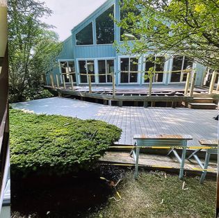 A blue A-frame house features a large, unfinished wooden deck under construction, with yellow caution tape bordering the area.
