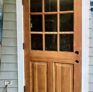 A wooden, nine-pane glass door installed in a light-colored house exterior.