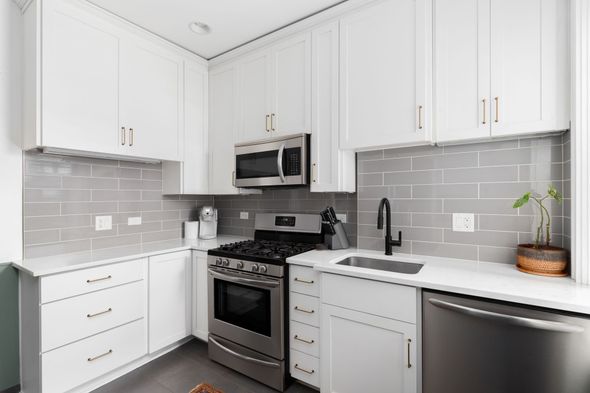A clean, modern kitchen with white cabinets, stainless steel appliances, grey subway tile backsplash, and white counters. A clean, modern kitchen with white cabinets, stainless steel appliances, grey subway tile backsplash, and white counters.