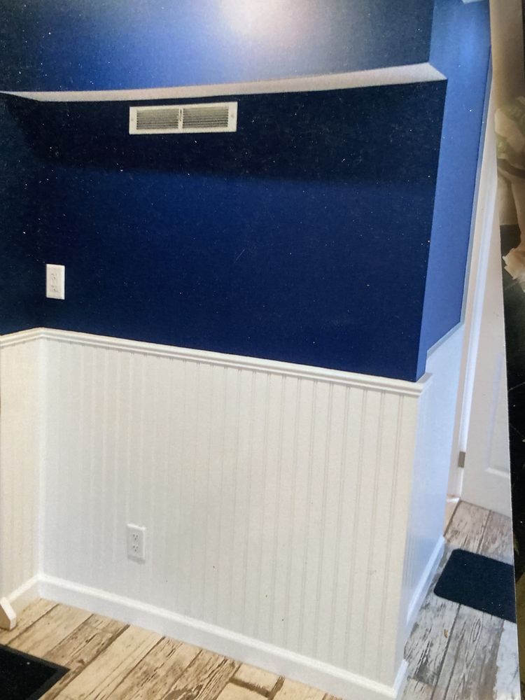 A wall with dark navy blue paint on top and white vertical beadboard paneling on the bottom, with a white air vent.