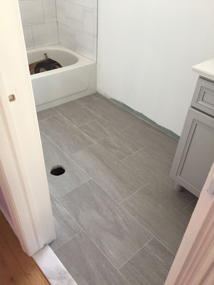 A partially renovated bathroom with grey wood-look floor tiles, a white bathtub, and a grey vanity cabinet. A partially renovated bathroom with grey wood-look floor tiles, a white bathtub, and a grey vanity cabinet.