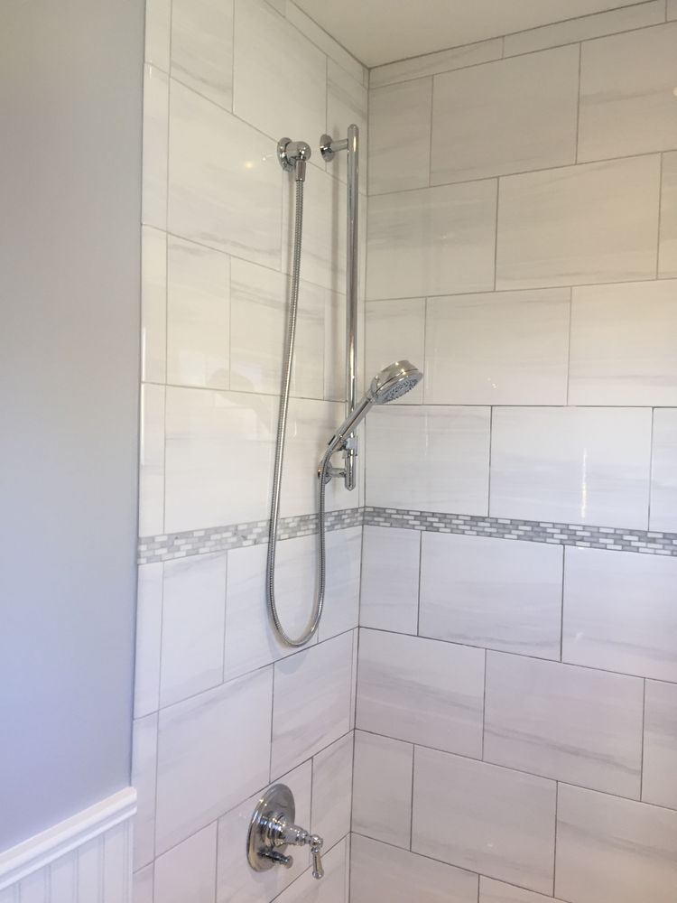 A chrome hand-held showerhead mounted on a vertical sliding bar in a shower with white marble-style tiled walls. A chrome hand-held showerhead mounted on a vertical sliding bar in a shower with white marble-style tiled walls.