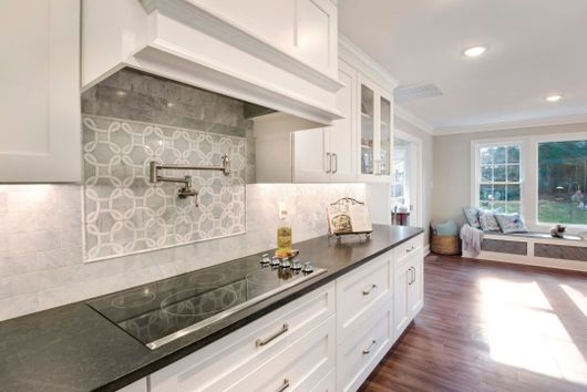 A kitchen with white cabinets and black counter tops and a stove top oven.