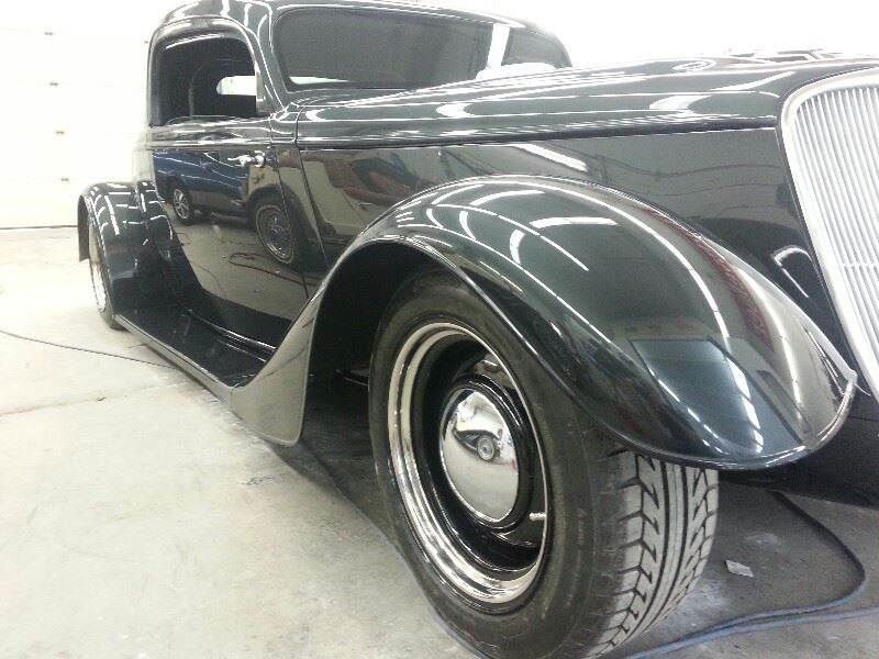 Dark green classic car with chrome wheels, side view.