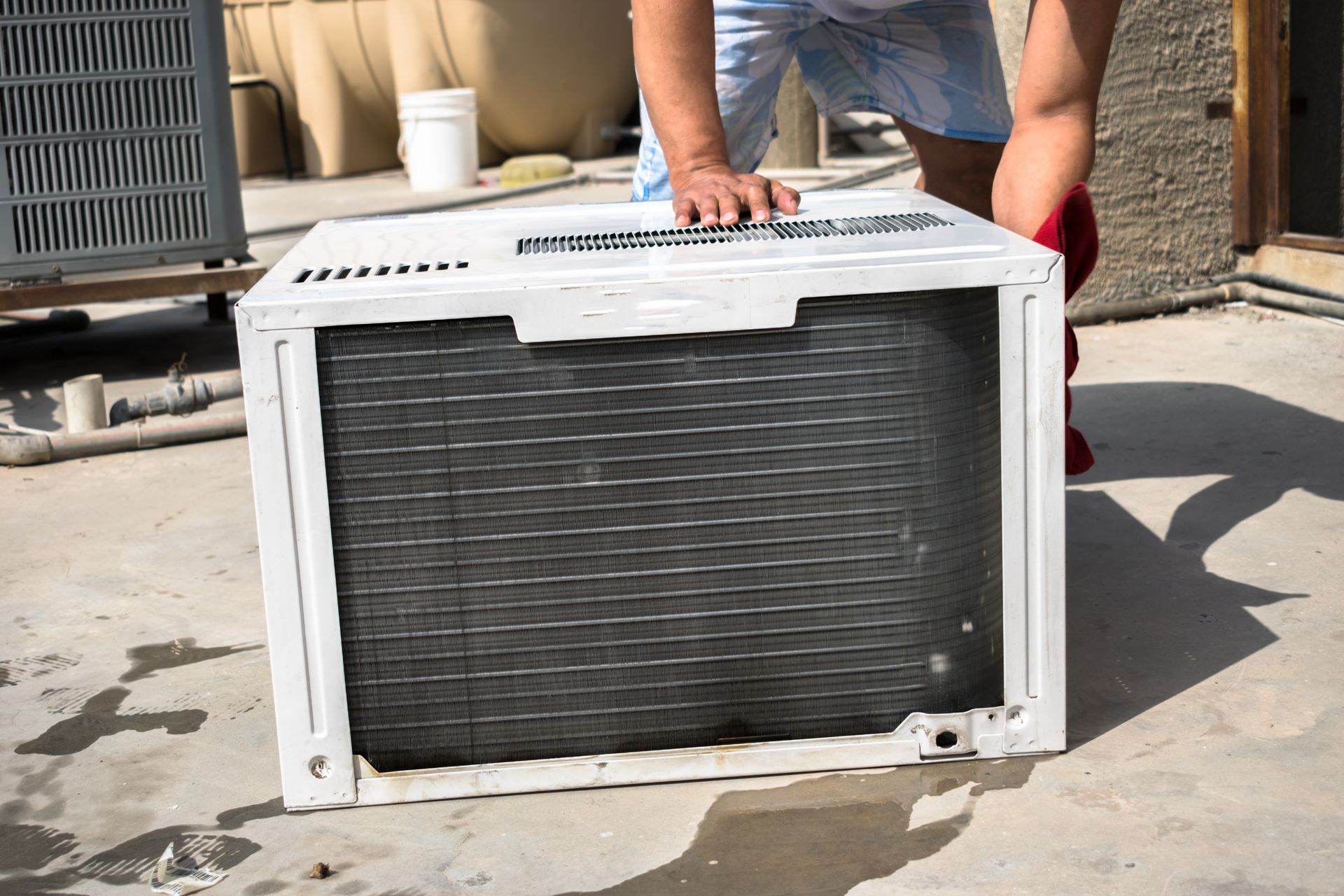 A person is cleaning an air conditioner on a concrete surface.