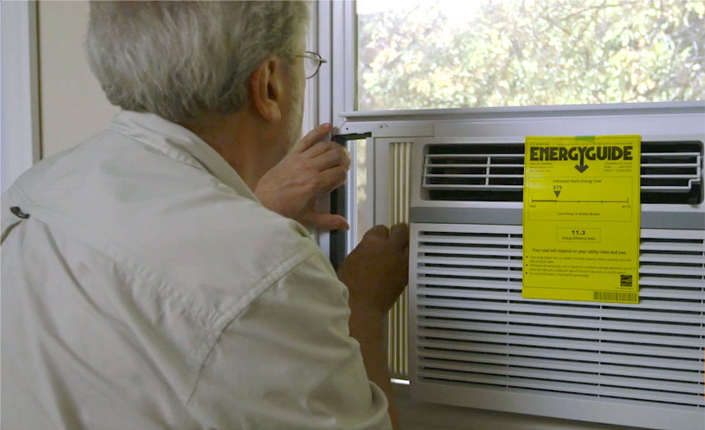 Man installing an air conditioner in a window, with an EnergyGuide sticker visible.