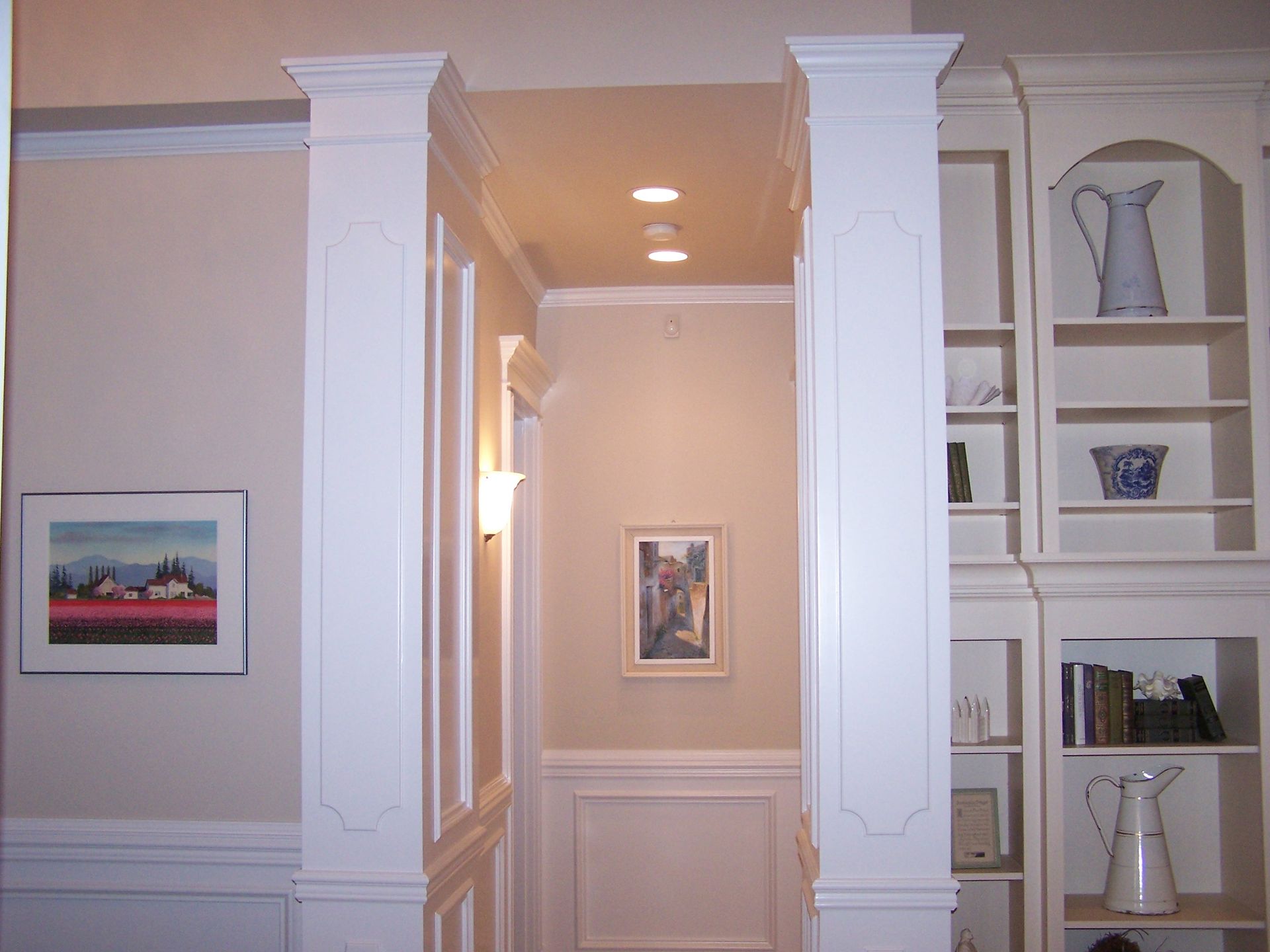 A hallway with white columns and shelves and a picture on the wall