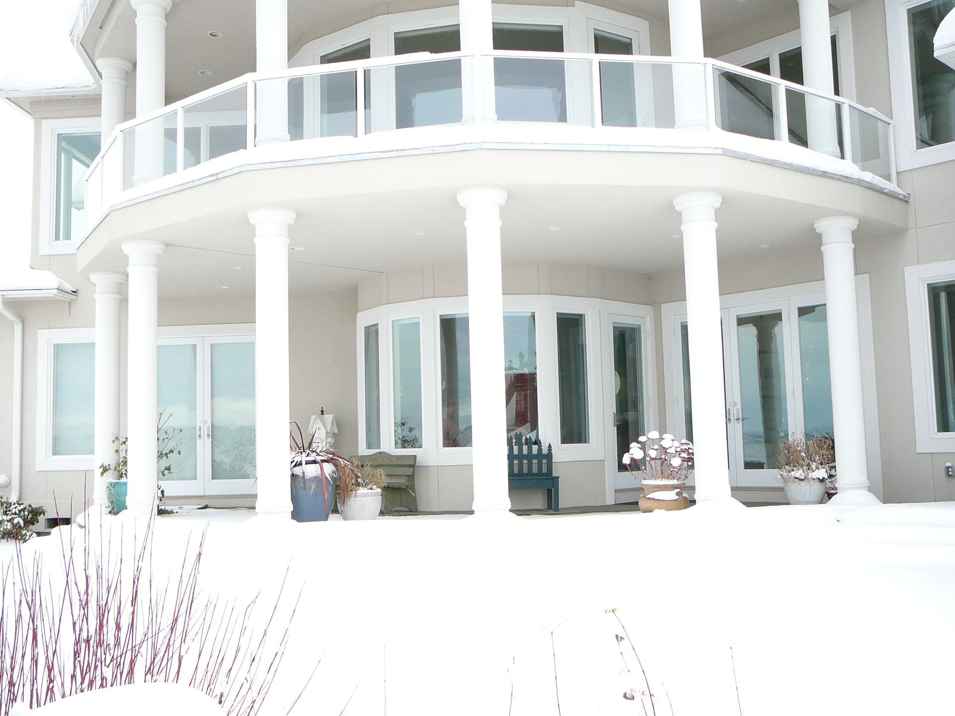 A large house with a balcony and columns is covered in snow.