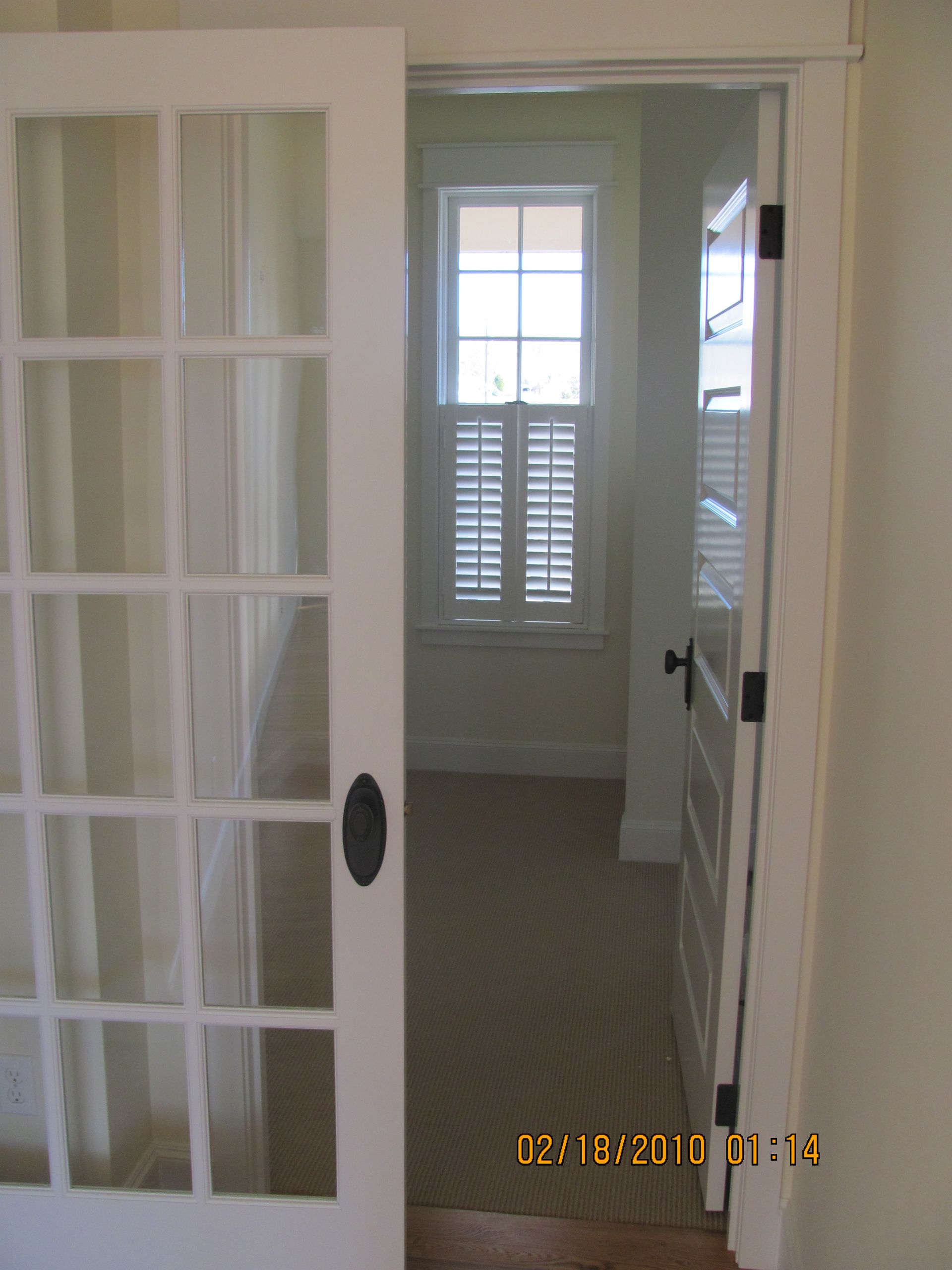 A french door is open to a room with shutters on the windows
