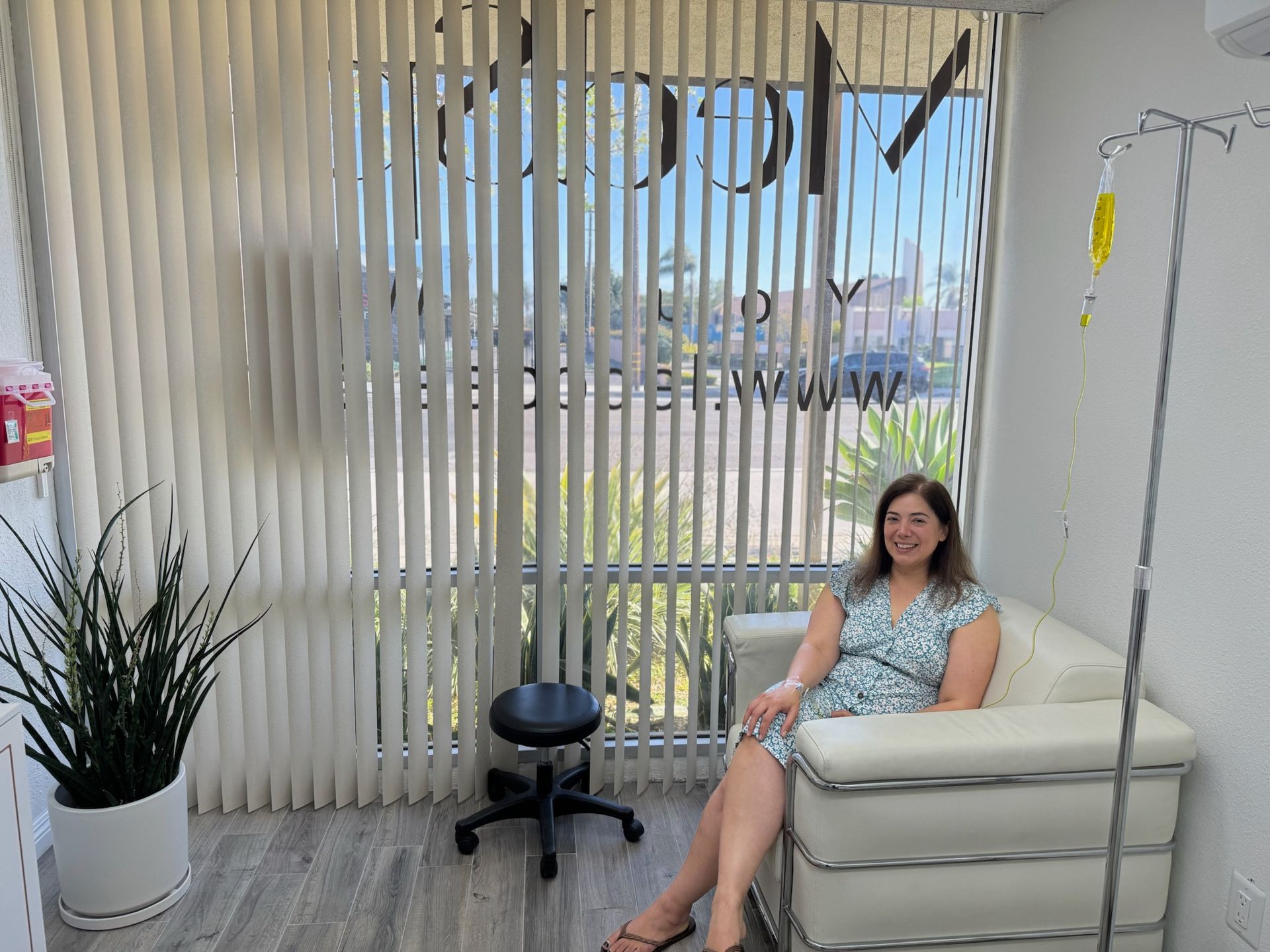 Woman in medical office sitting near a window and IV drip stand.