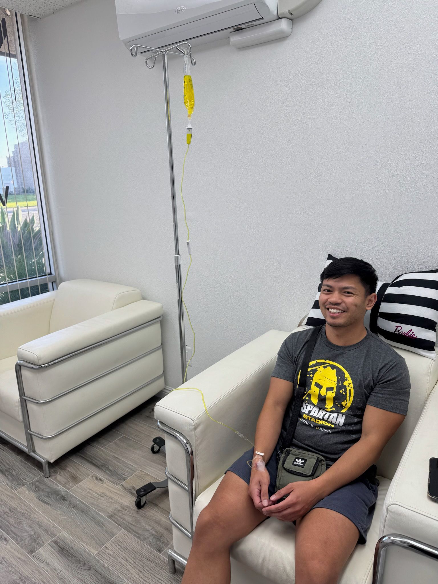 Smiling man getting IV fluids, seated on white chair; bright, modern room.