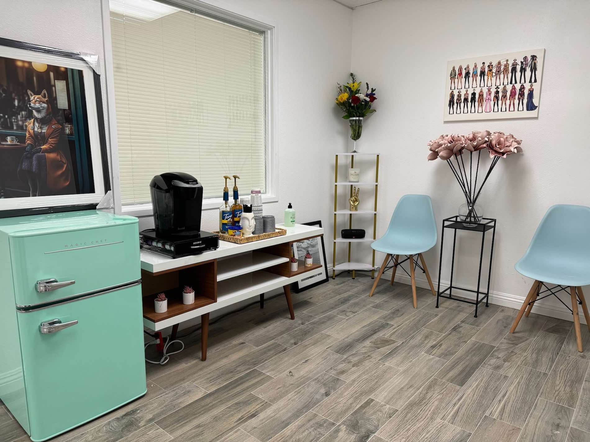 A waiting room with a green refrigerator , chairs , a table and a window.