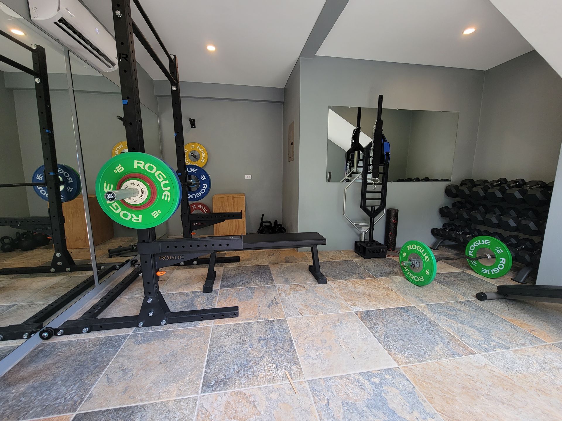 A gym with a bench , barbells , and a mirror.