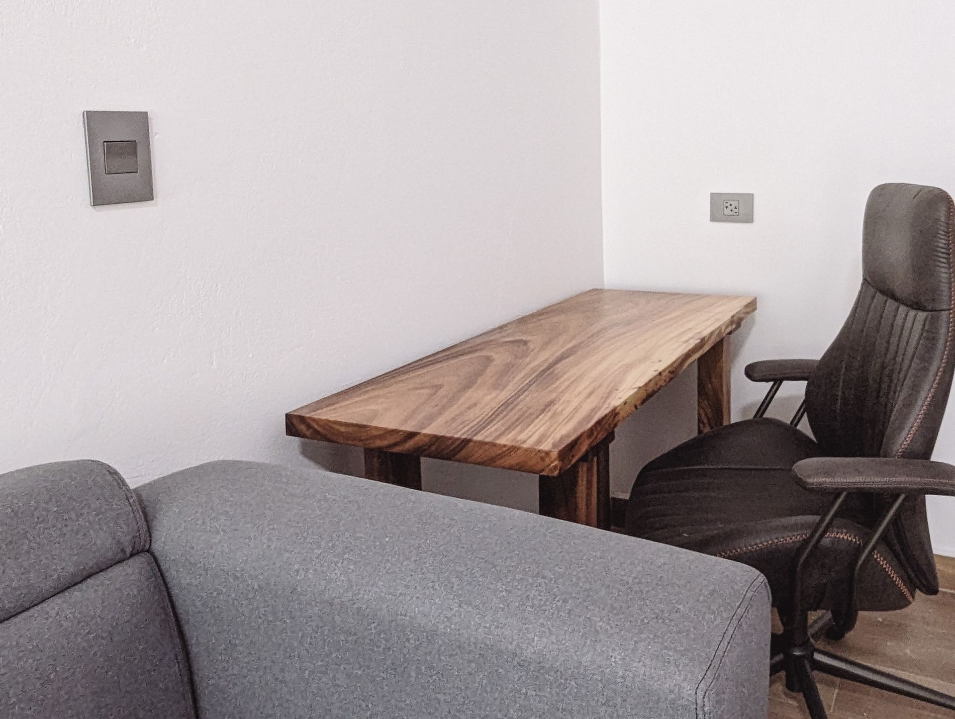 A chair is sitting next to a wooden desk in a living room.