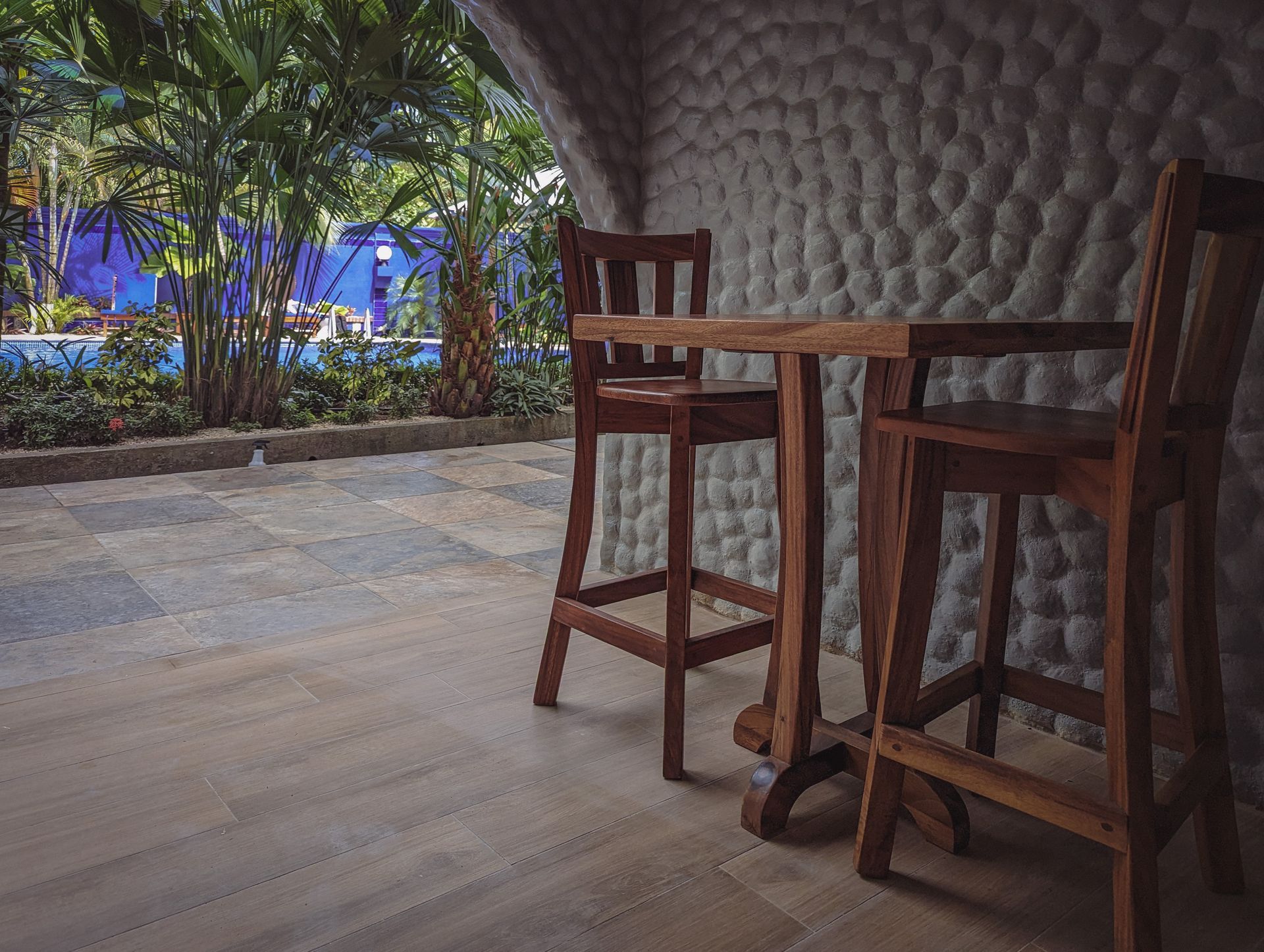 A wooden table and chairs are sitting on a patio next to a stone wall.