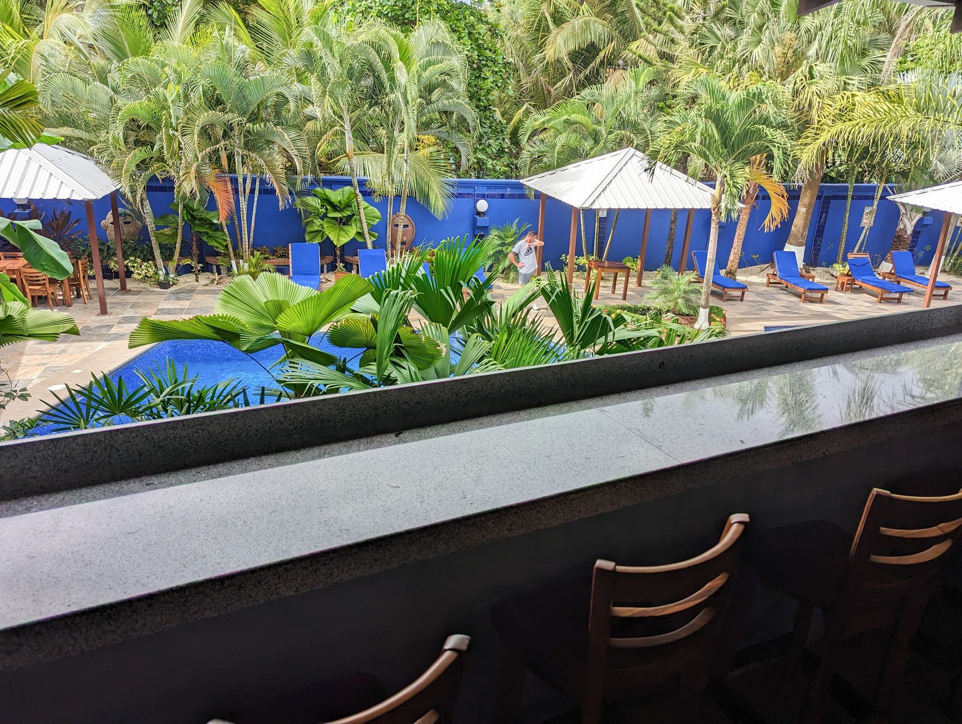 A view of a pool from a balcony with umbrellas and chairs.