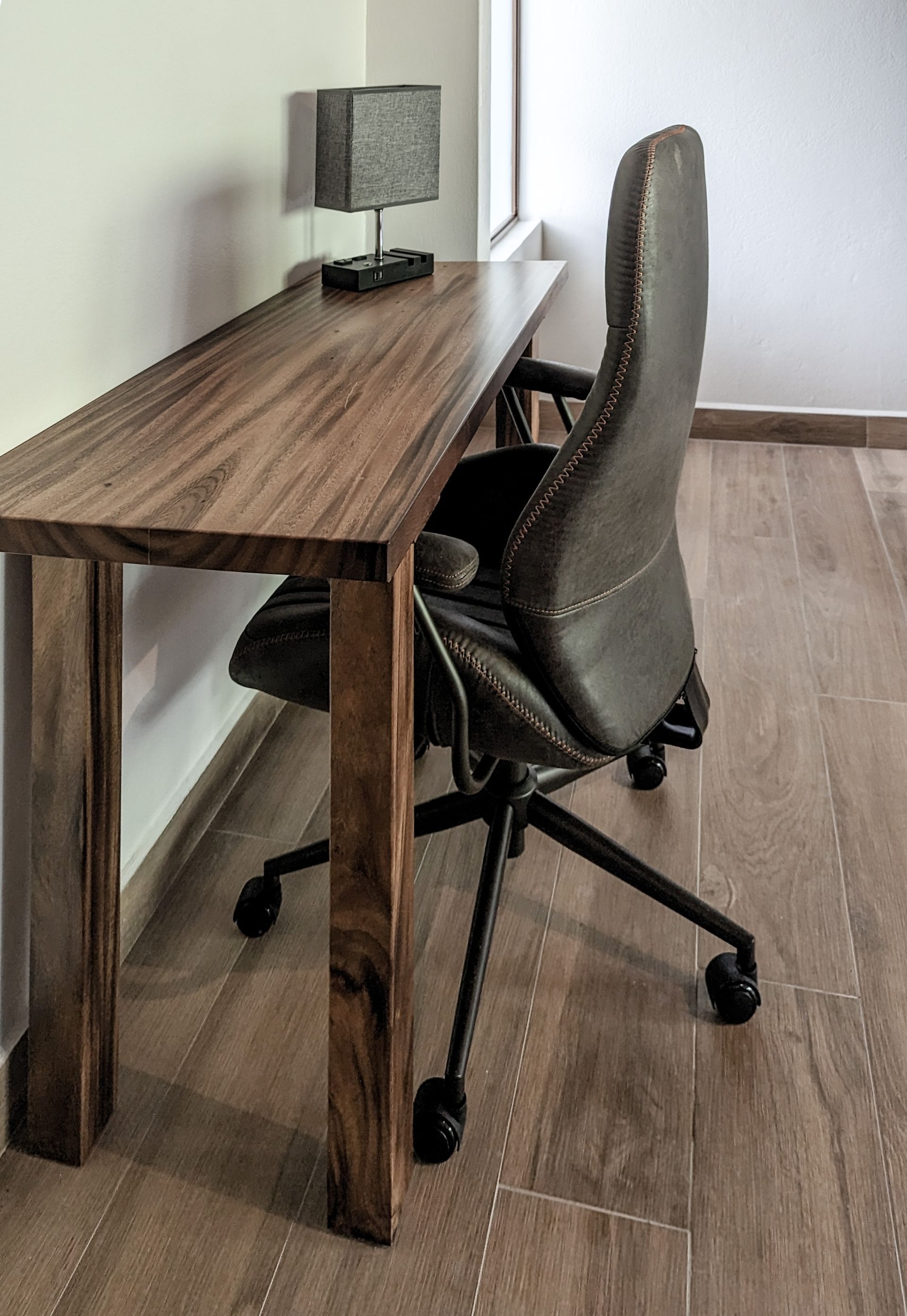 A chair is sitting next to a wooden desk in a room.