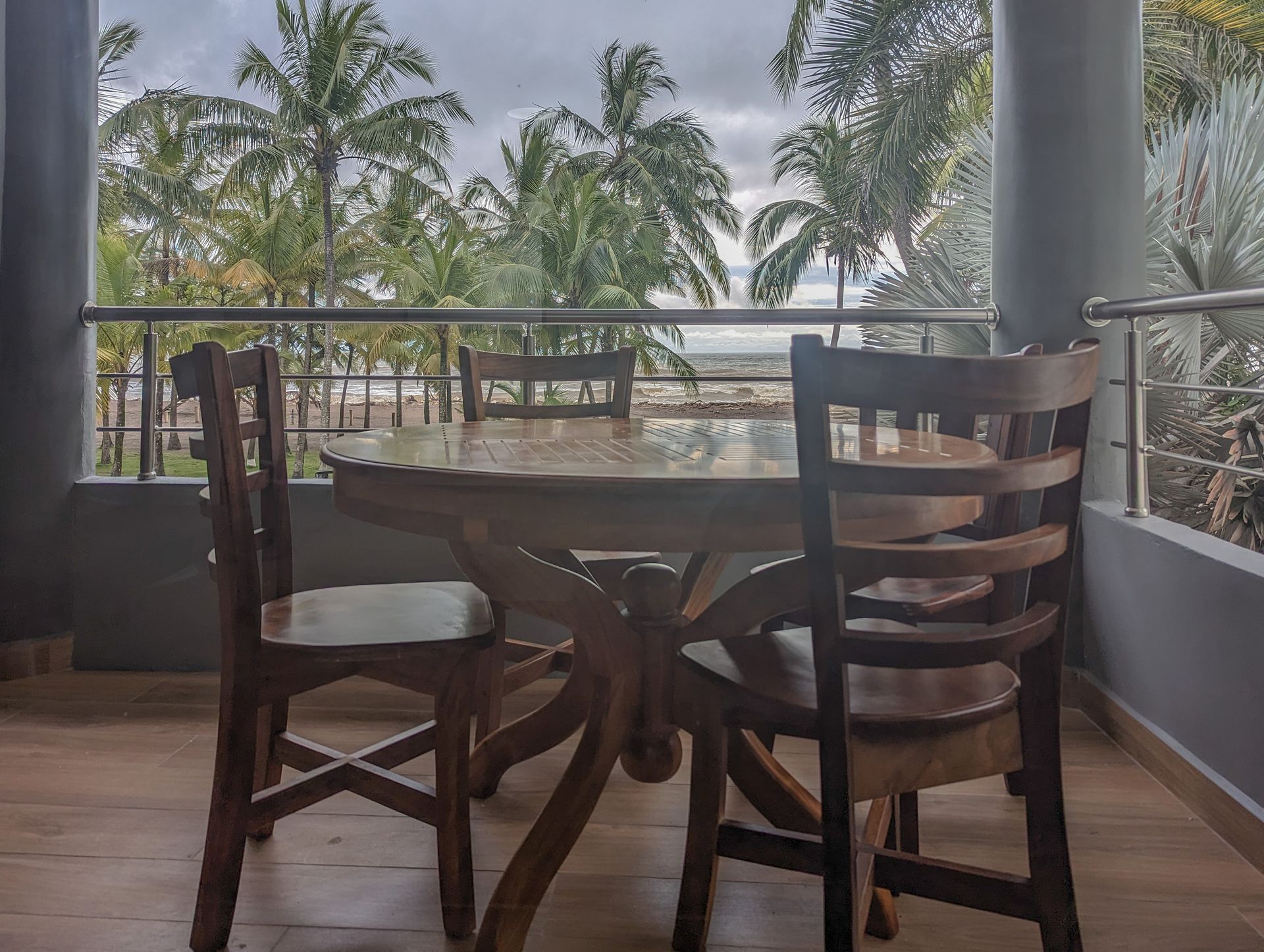 A table and chairs on a balcony with a view of palm trees.