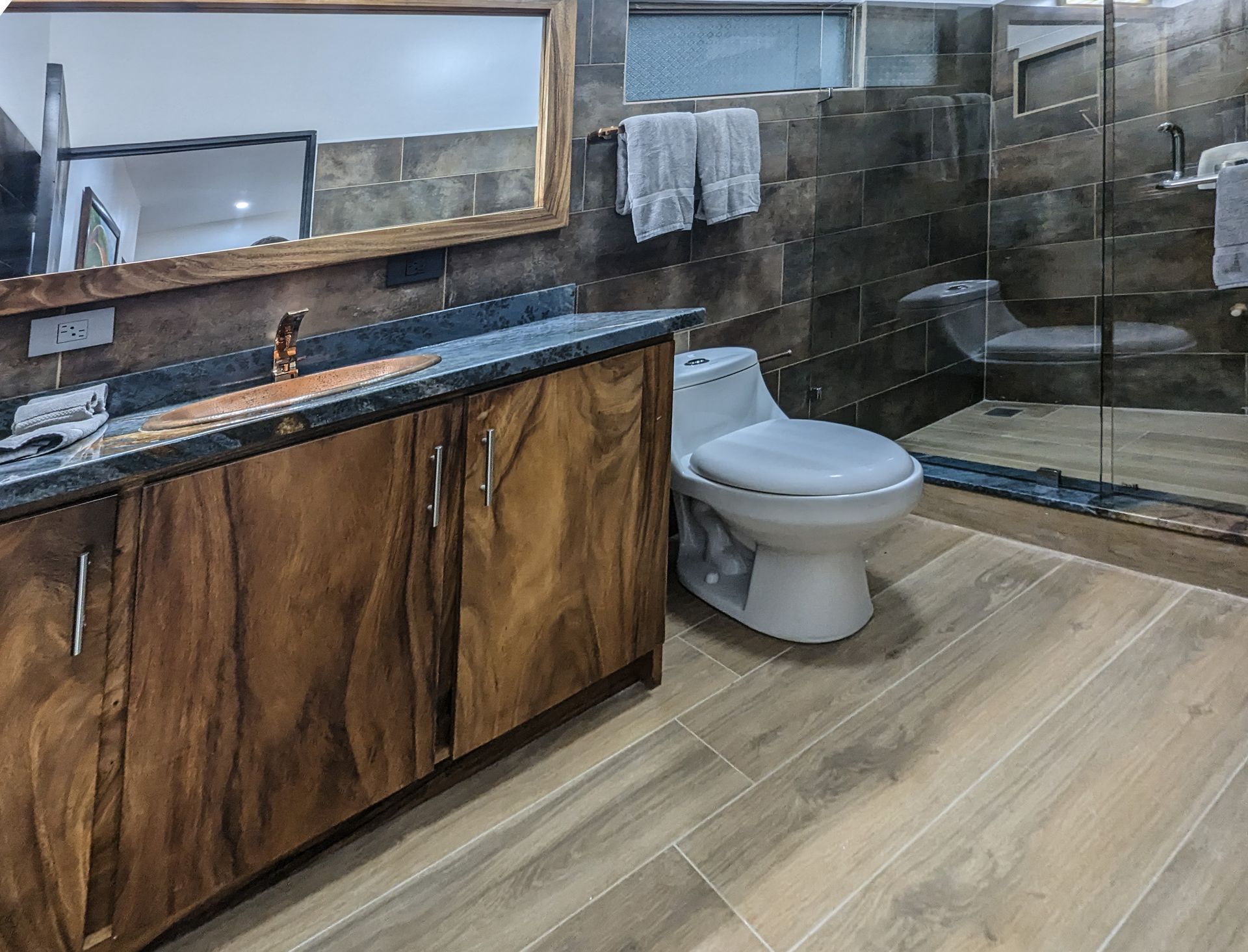 A bathroom with a toilet , sink , mirror and walk in shower.