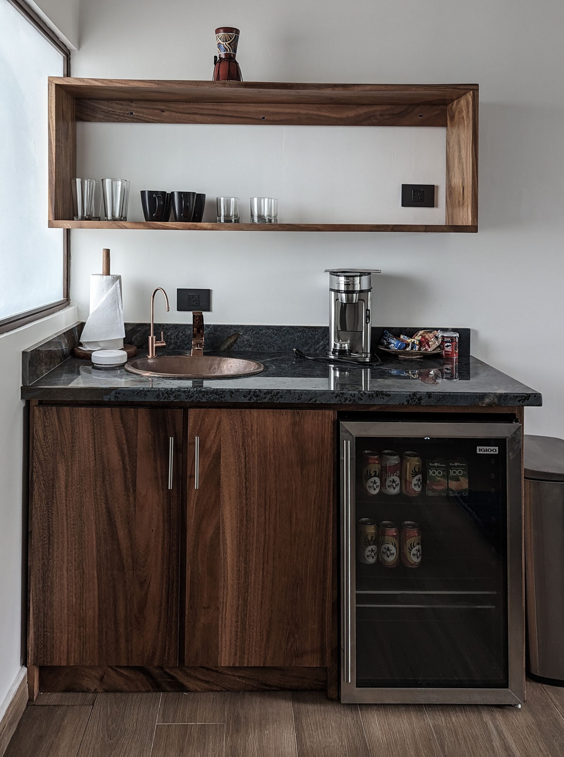 A kitchen with wooden cabinets , a sink , a refrigerator and a shelf.