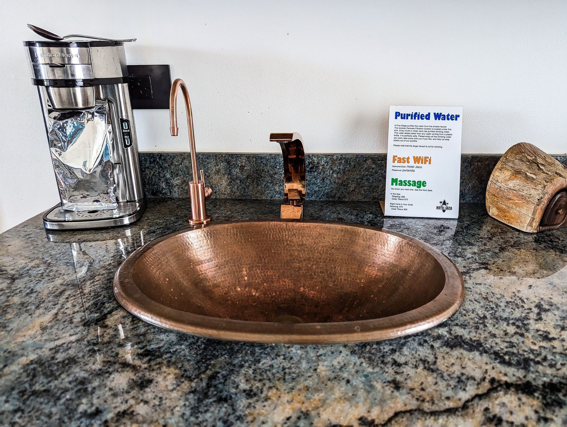 A copper sink sits on a granite counter next to a coffee maker