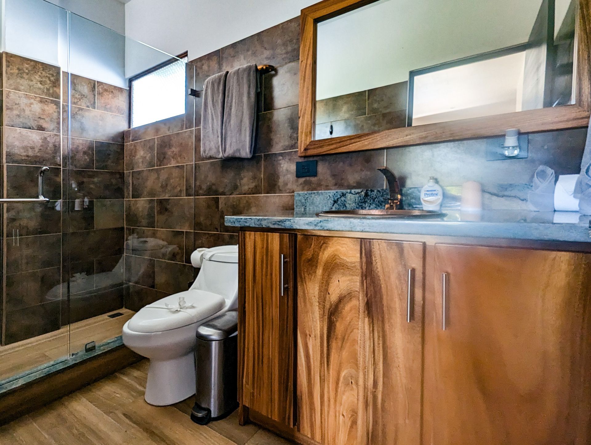 A bathroom with a toilet , sink , mirror and walk in shower.