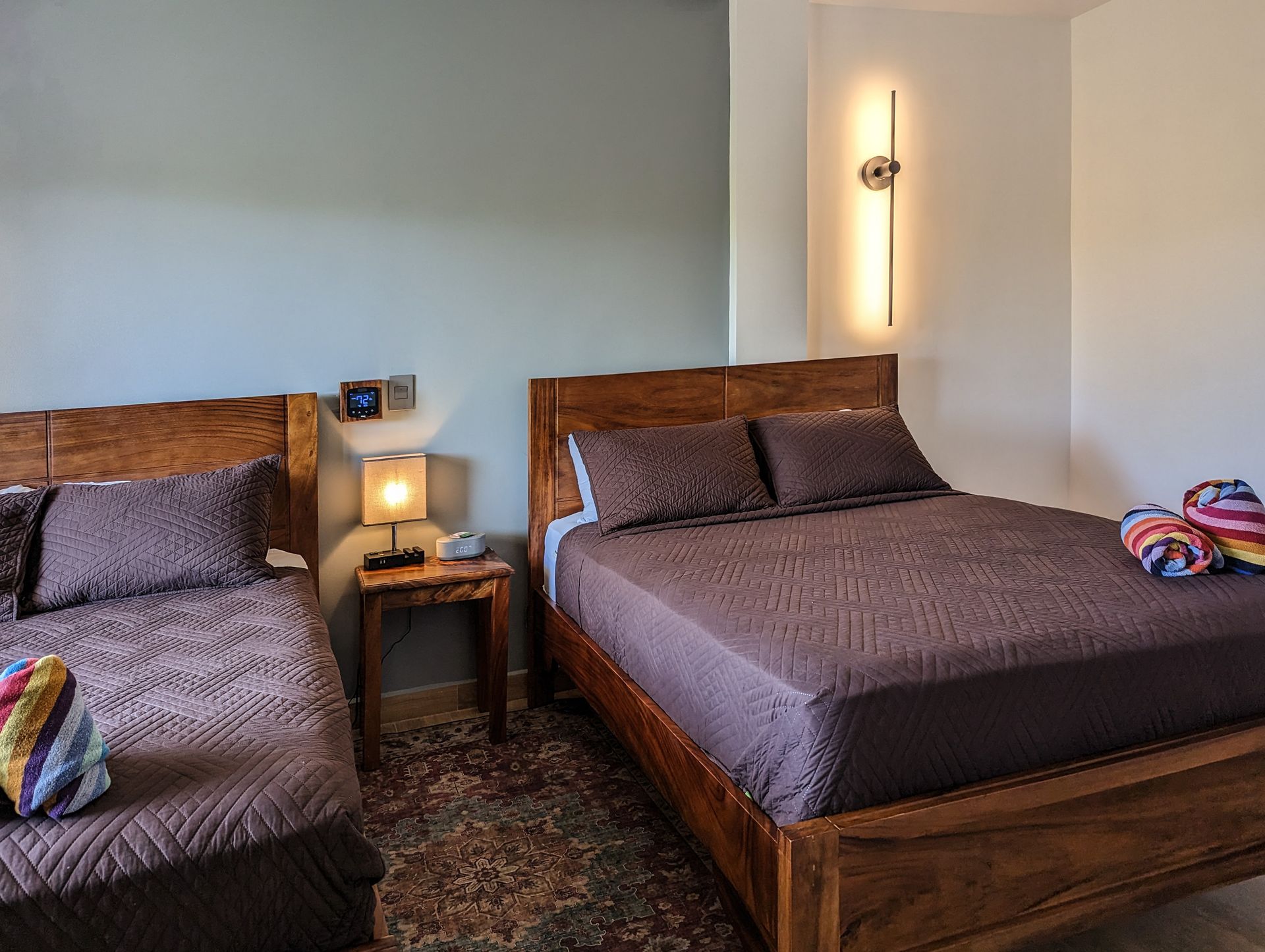 A bedroom with two beds and a lamp on the wall.