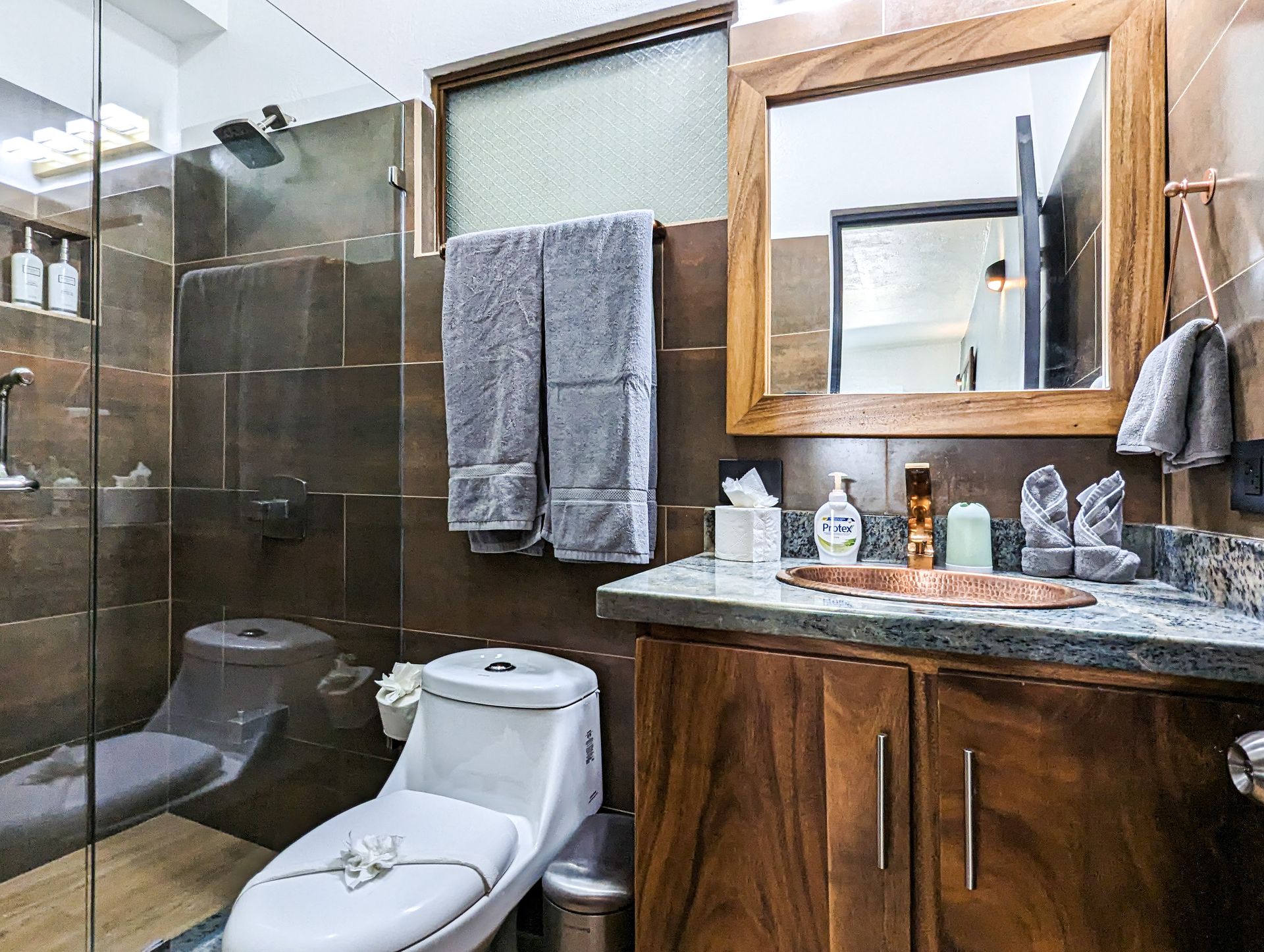 A bathroom with a toilet , sink , mirror and shower.