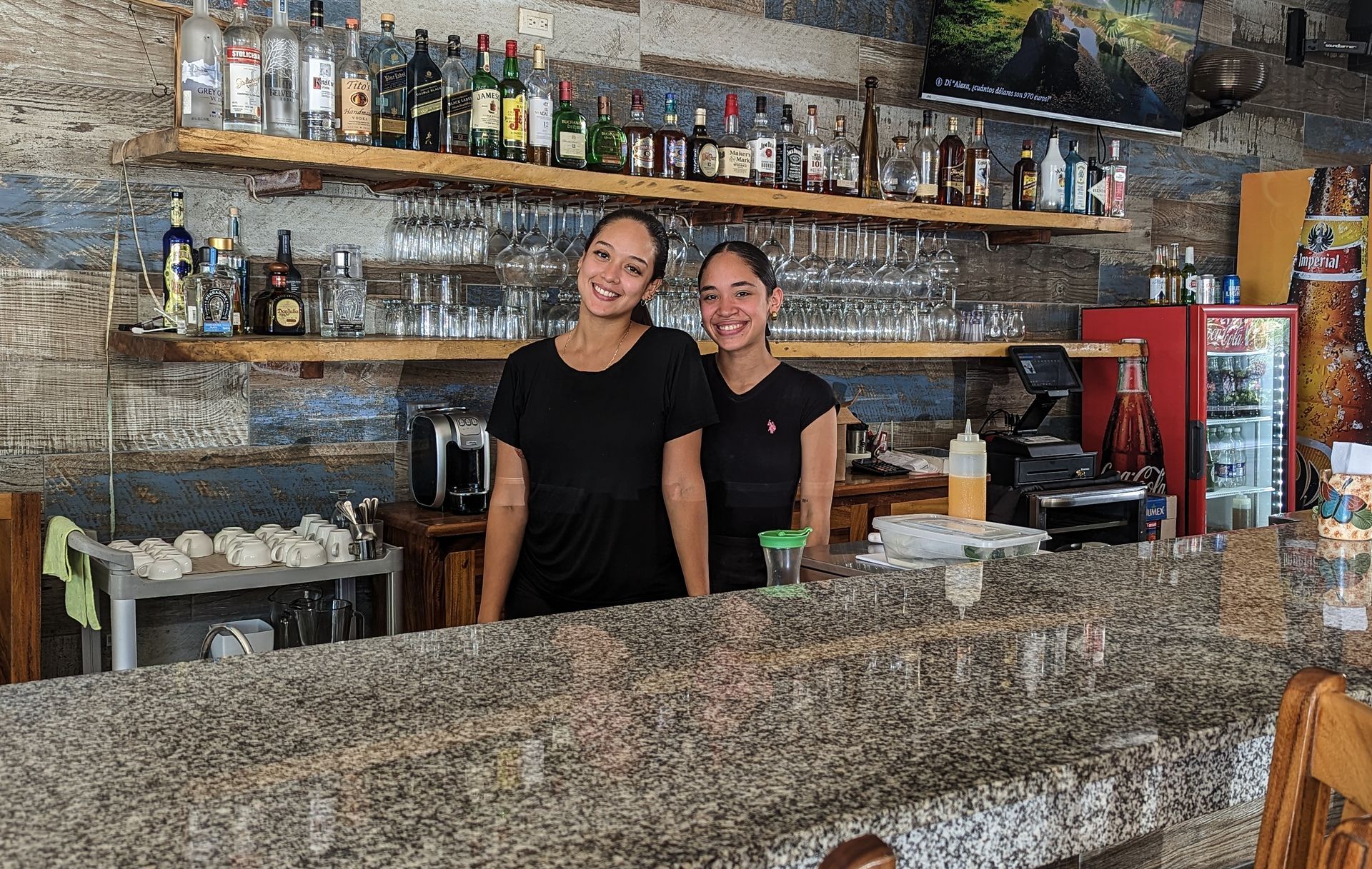 Two women are standing behind a bar in a restaurant.