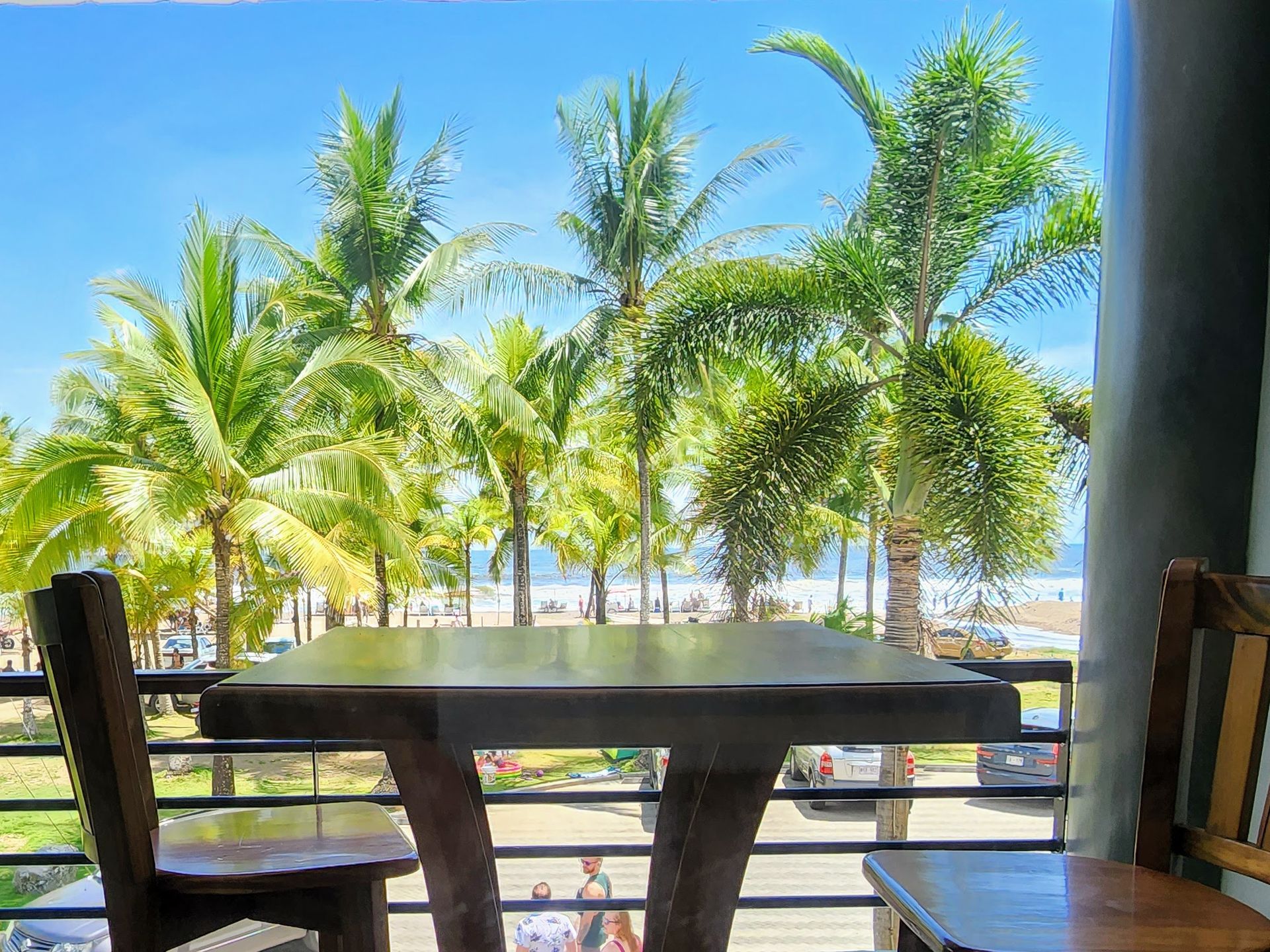 A table and chairs on a balcony with a view of palm trees and the ocean.