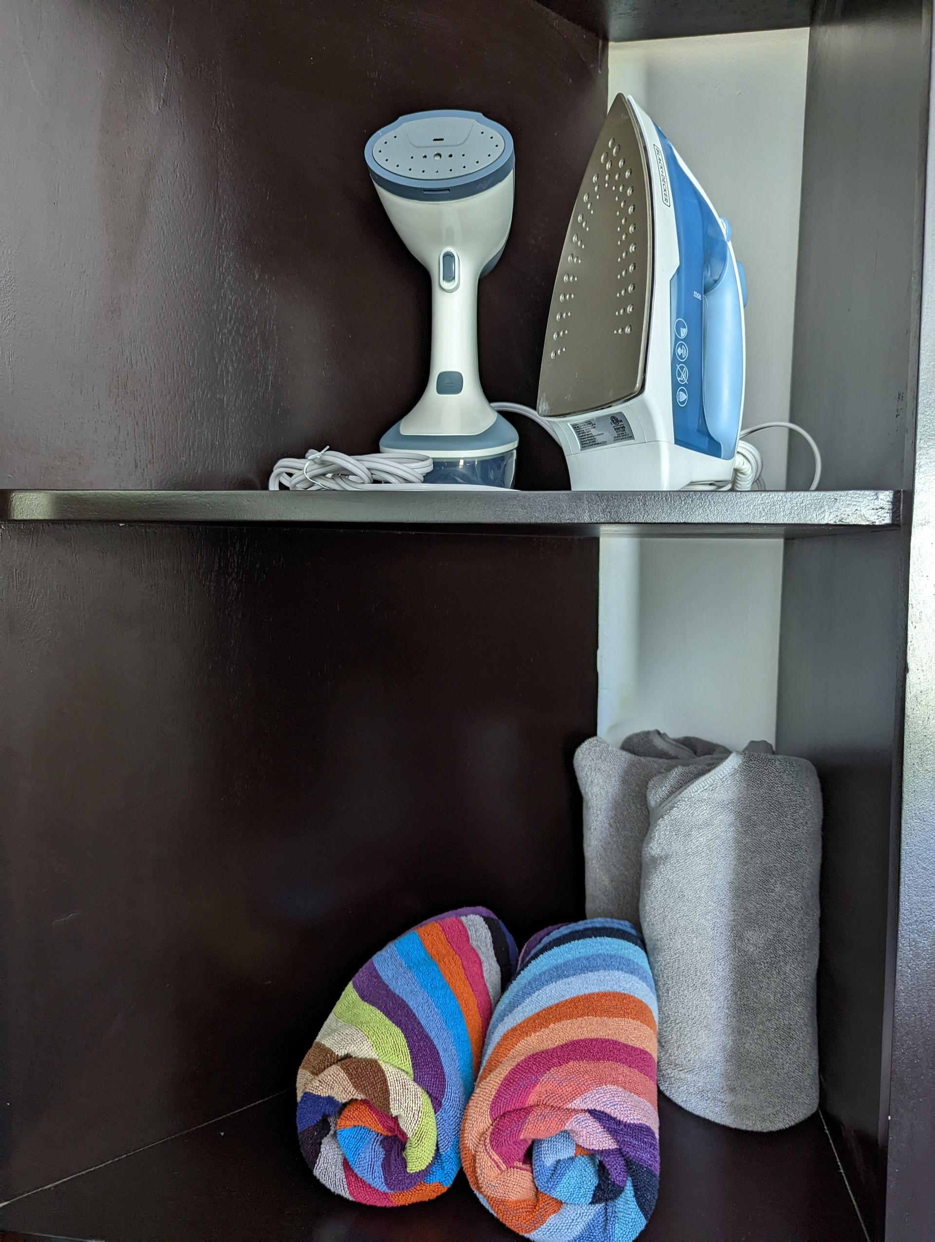 A shelf with a vacuum cleaner , iron , and towels on it.