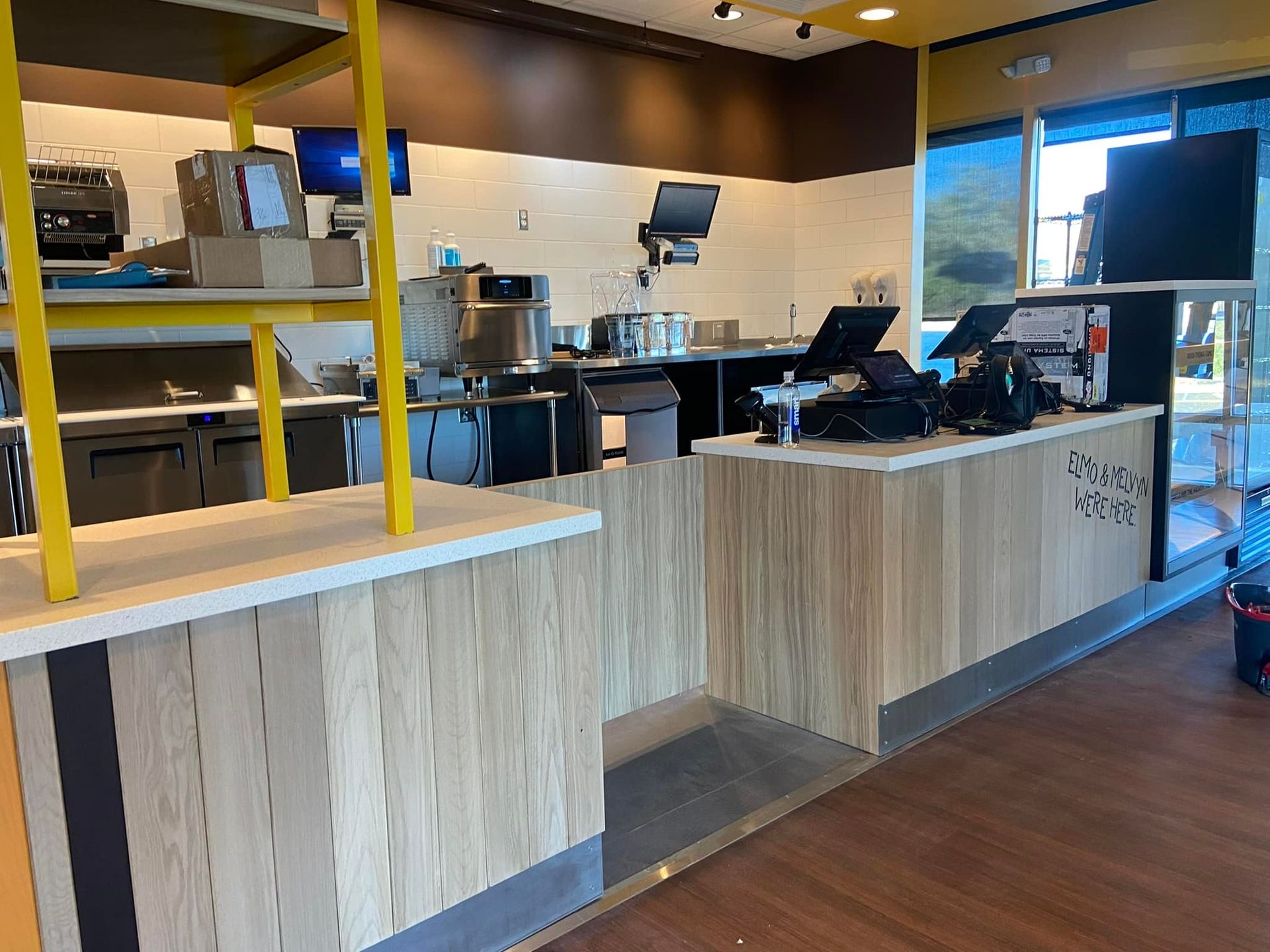 Interior of a restaurant with a light wood counter, POS system, and kitchen appliances.