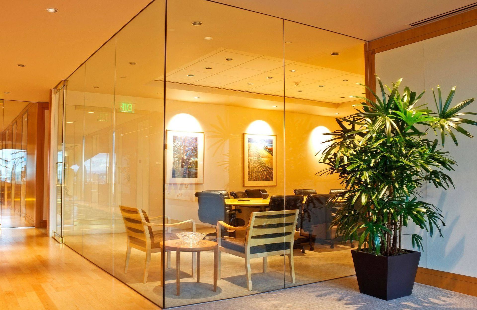 Glass-walled office with wooden accents, chairs, table, and plant, bathed in warm lighting.