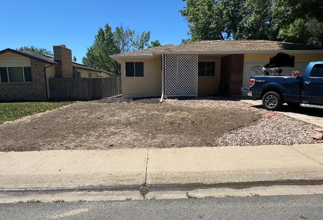 Brown yard in front of a tan house with a blue truck parked in the driveway.