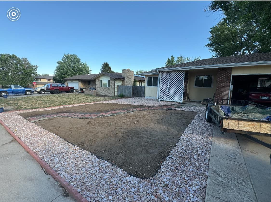 Front yard with brown dirt bed framed by light-colored rocks, a house, and a blue sky.