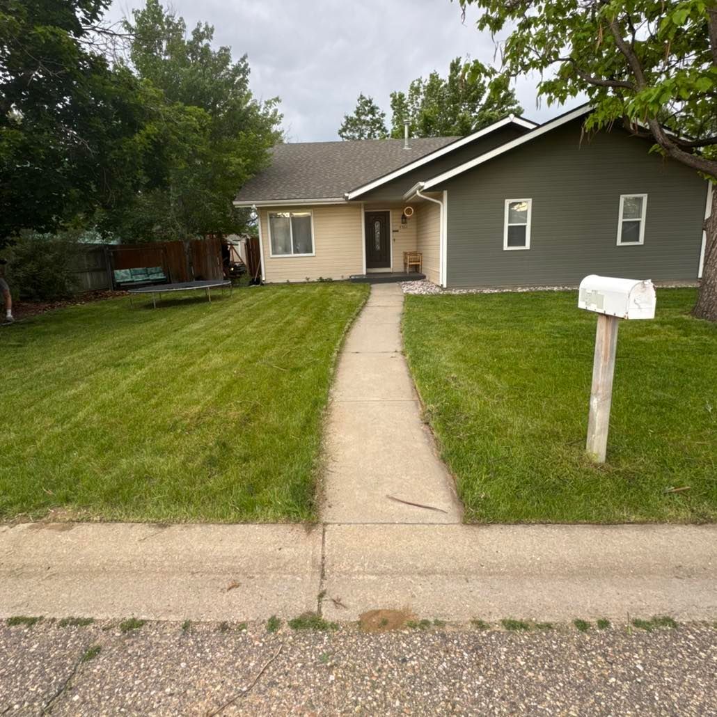 A house with beige and grey siding, a green lawn, and a sidewalk leading to the front door.