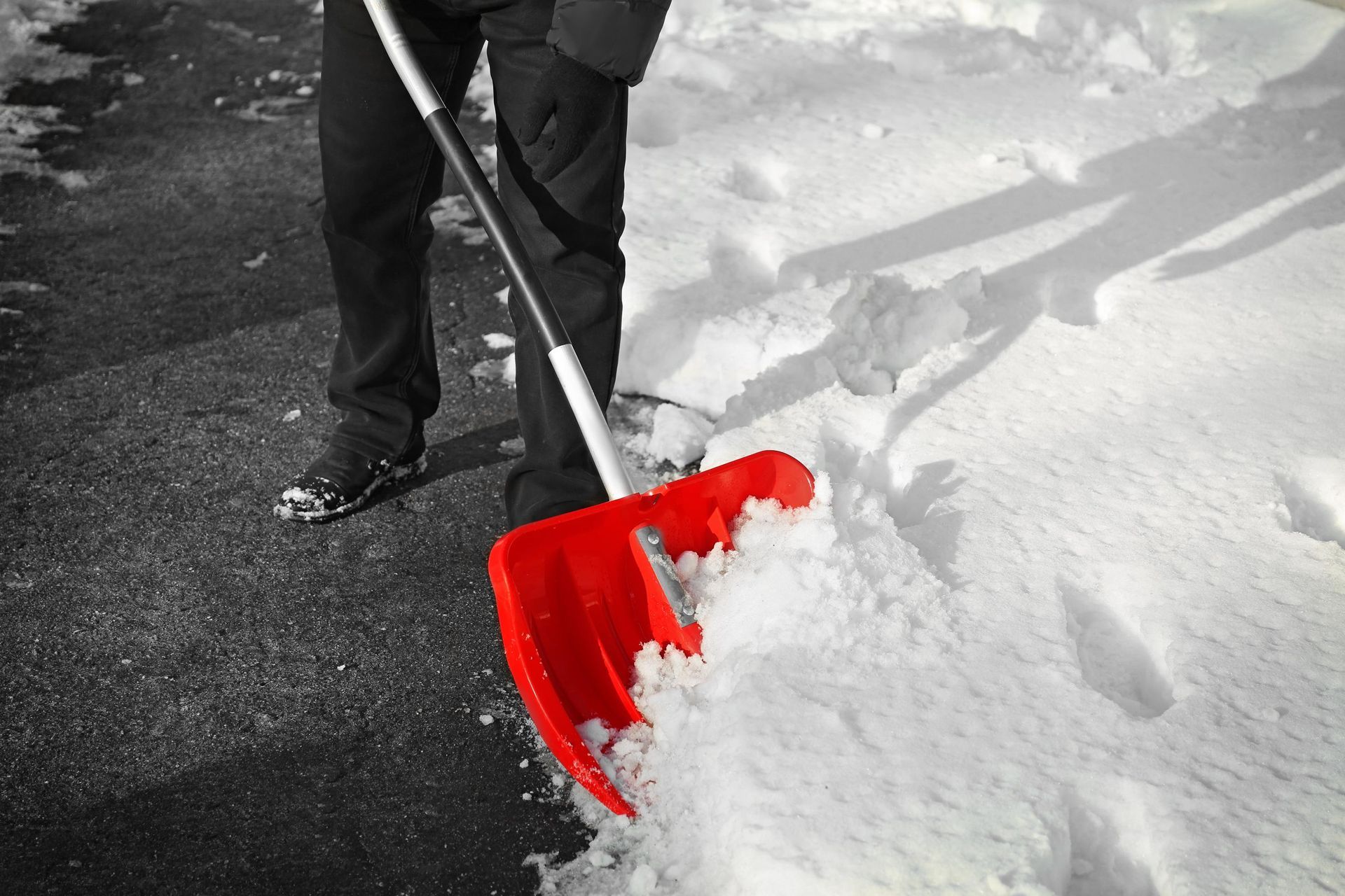 Person shoveling snow from a dark asphalt surface using a red shovel.