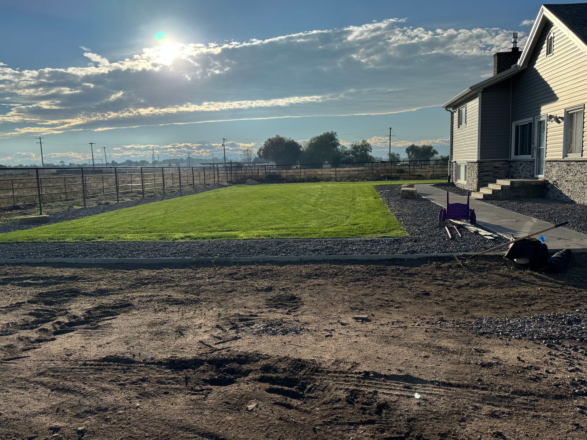 A house with a green lawn, dirt, and a gravel border on a sunny day.