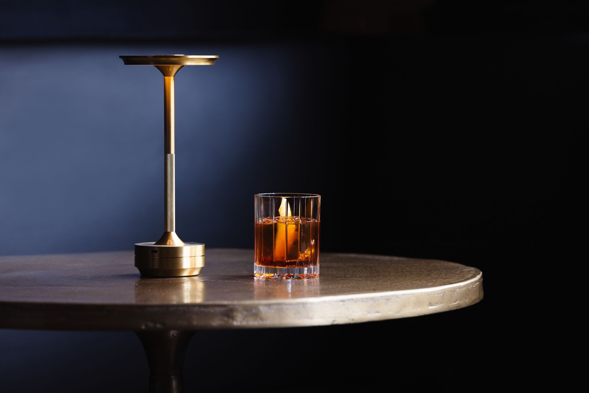 A glass of whiskey sits on a table next to a lamp
