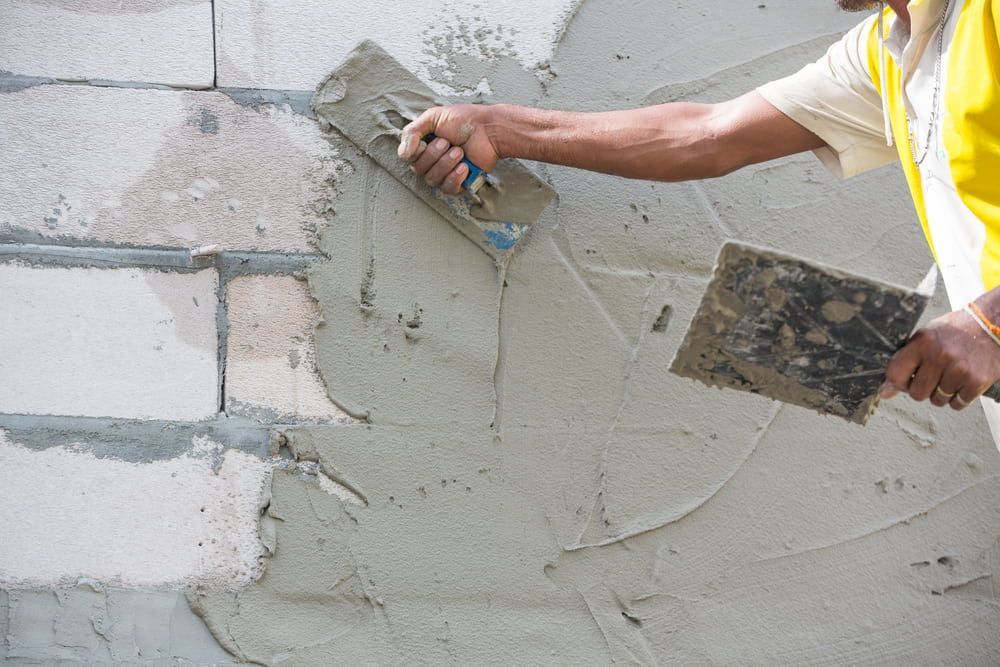 A Man Is Plastering a Wall with A Trowel — MJ Watson Construction and Maintenance in Wagga Wagga, NSW