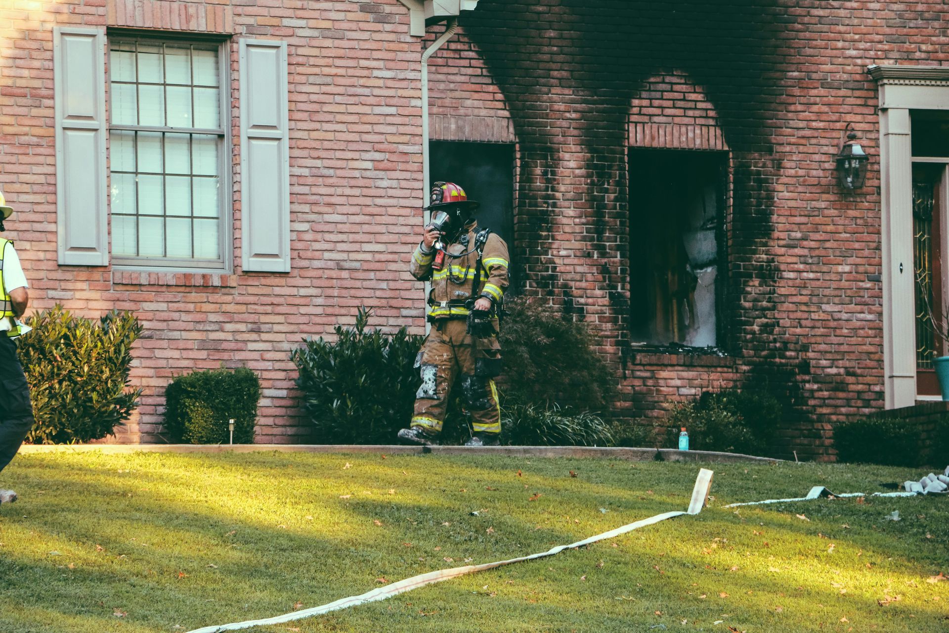 Fire fighter coming out a burnt house with a hose.