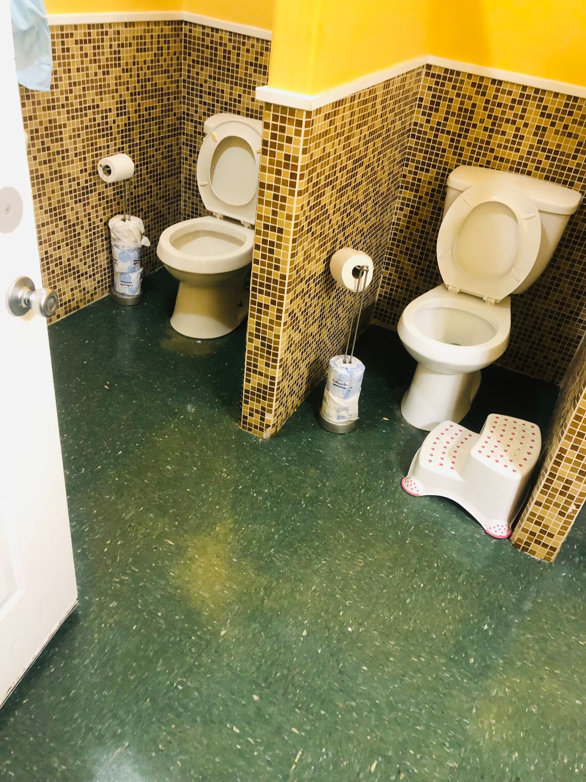 a bathroom with two toilets and a step stool